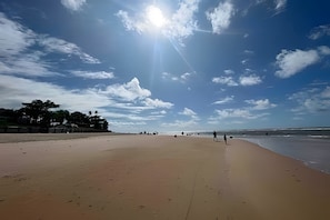 Una playa con cielo despejado, algunas personas caminando y un mar tranquilo.