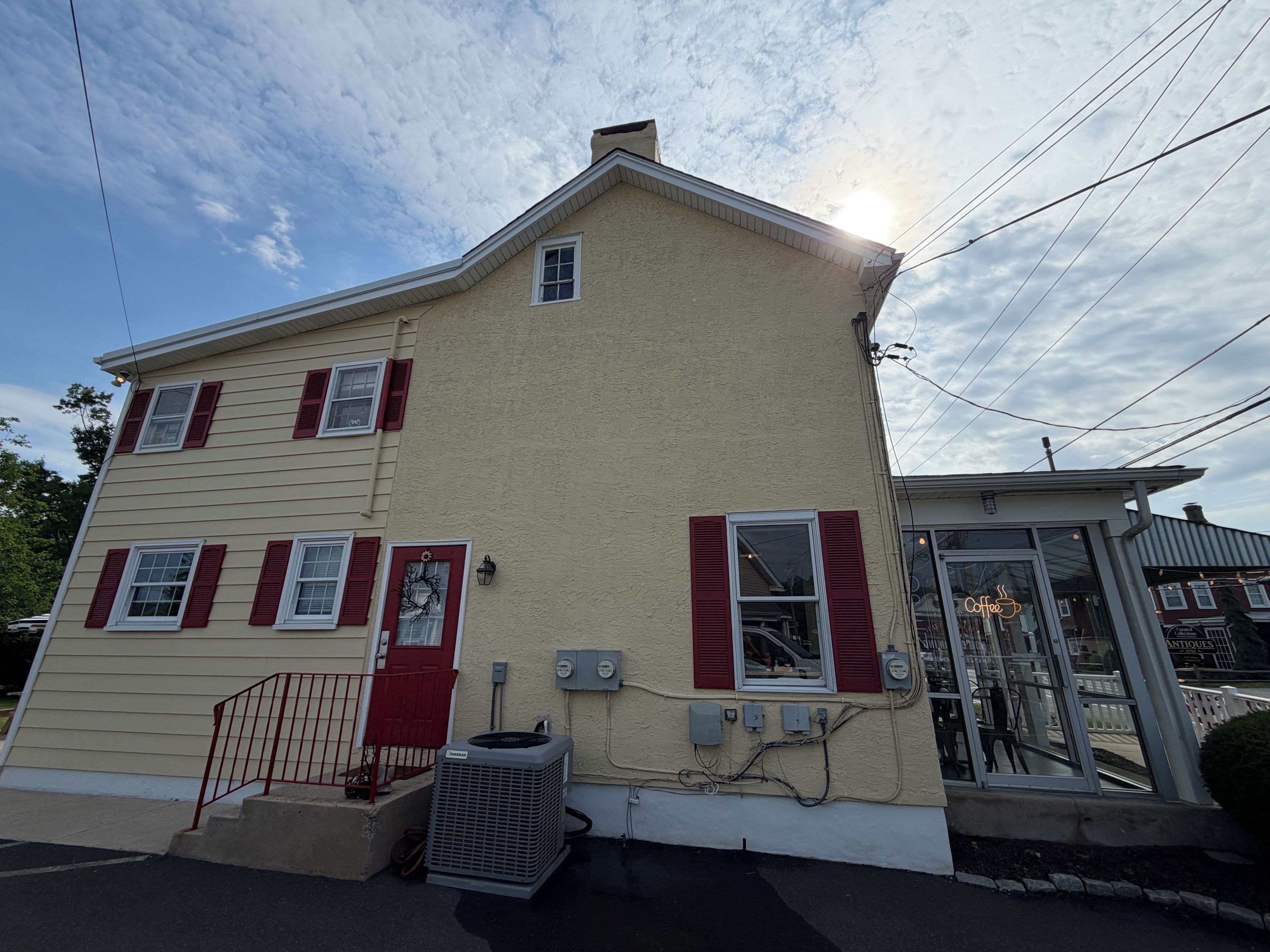 A two-story house with a beige exterior and red shutters, a front door, and an air conditioning unit.