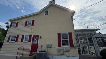 A two-story house with a beige exterior and red shutters, a front door, and an air conditioning unit.