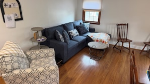 A living room with a sofa, armchair, small round table, and a wooden chair.