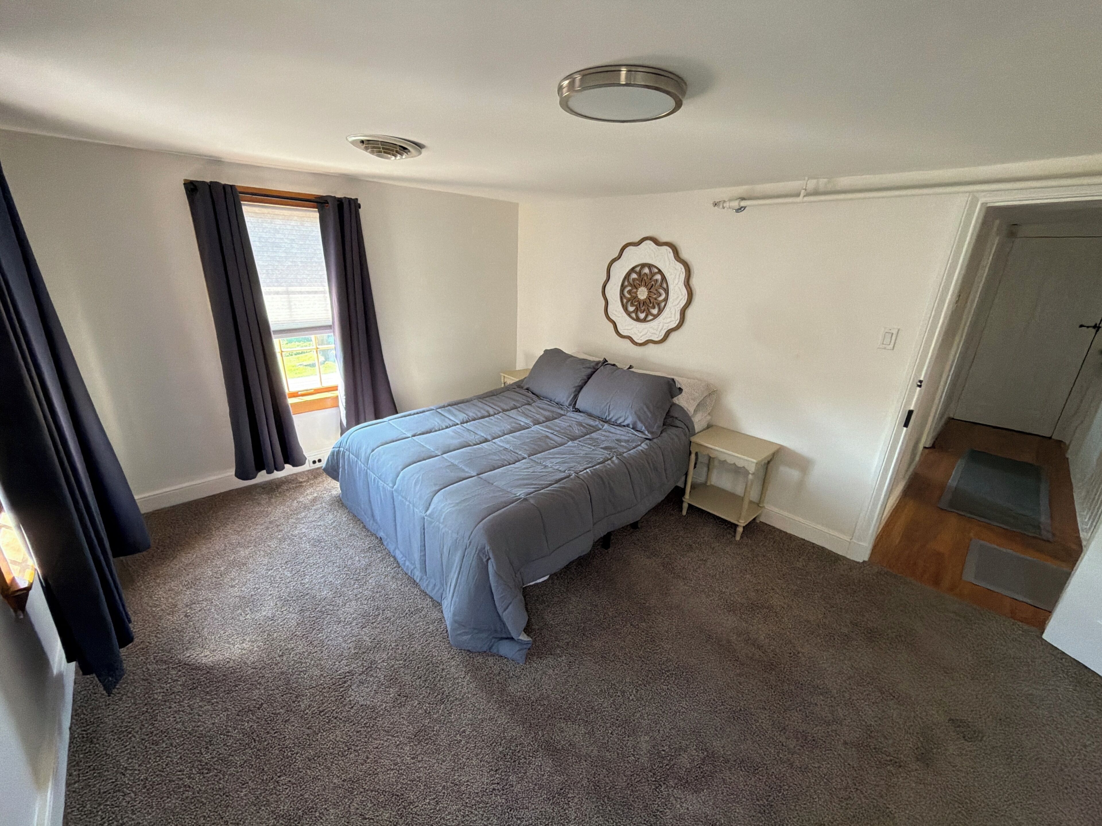 A bedroom with a bed, a nightstand, a decorative wall piece, and a door.