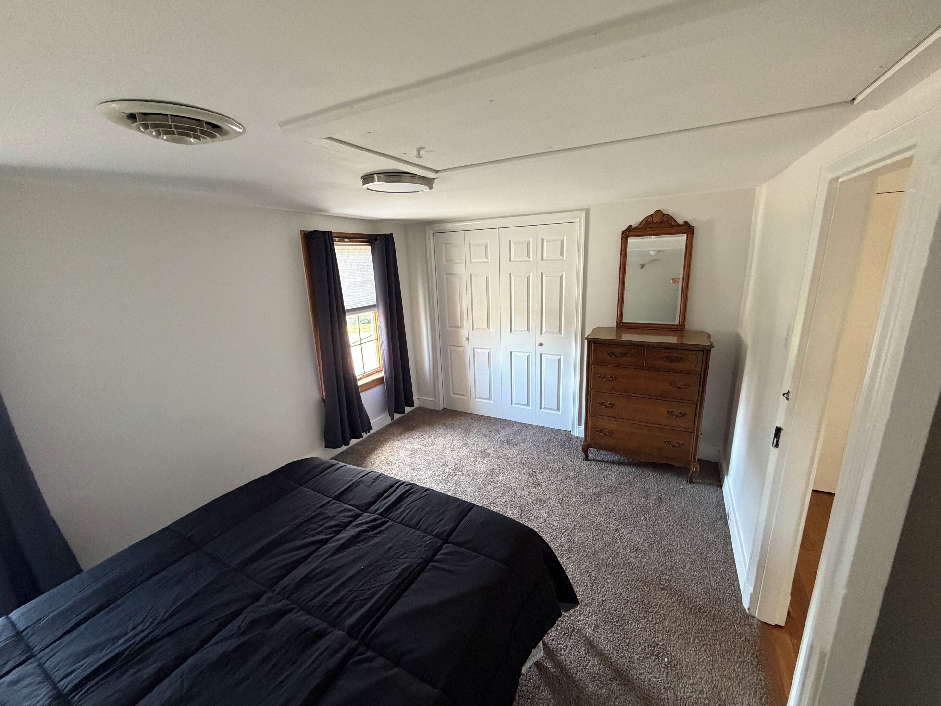 A bedroom with a bed, dresser, mirror, and a door leading to another room.