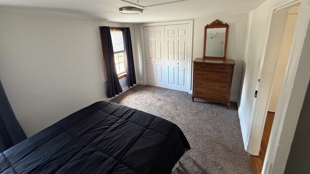 A bedroom with a bed, dresser, mirror, and a door leading to another room.