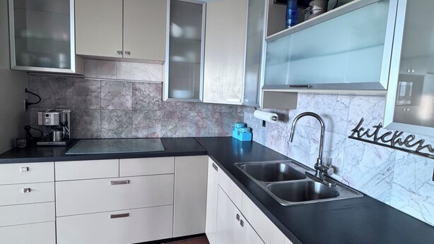 Una cocina moderna con armarios blancos, encimera negra y salpicadero de mármol.