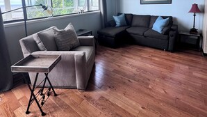Una sala de estar con sofá, una mesa de centro de madera y un ventanal con vistas a la vegetación.