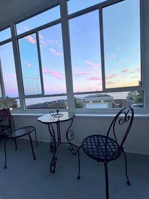 A room with a large window overlooking a cityscape, two metal chairs, and a small table with a heart-shaped decoration.