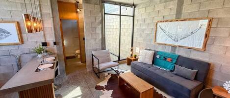 A modern interior with a kitchen, dining area, and living space featuring a cowhide rug, a sofa with cushions, and a hanging artwork.