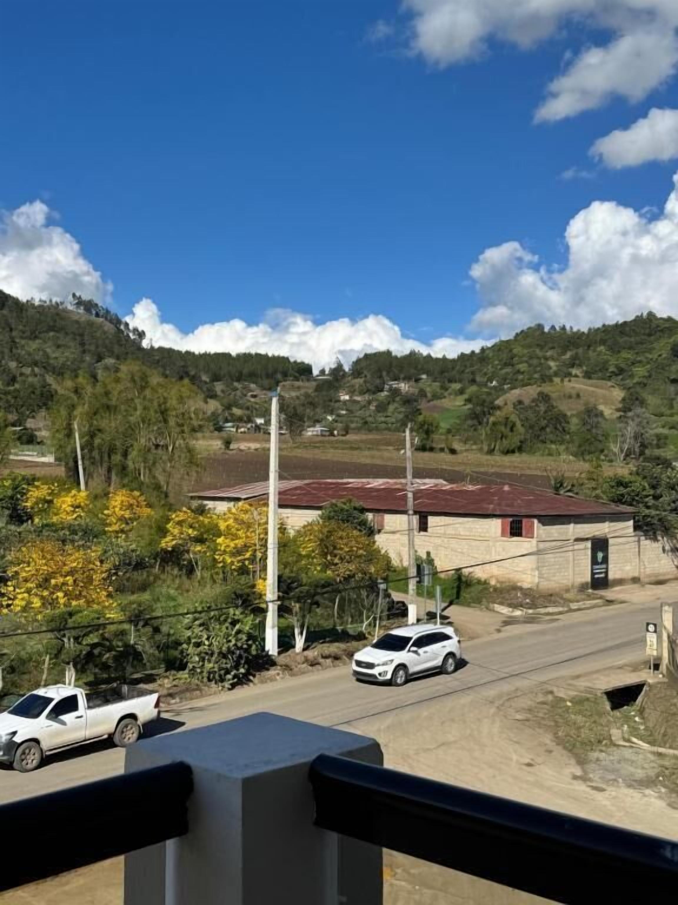 Un paysage rural avec une route, une voiture blanche et un bâtiment doté d’un toit rouge.