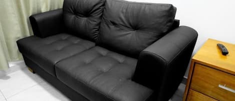 A black leather sofa with a wooden side table and a drawer unit.
