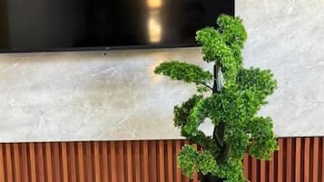 Une plante en pot est posée sur une table en bois, adossée à un mur composé de lattes de bois verticales, et un grand téléviseur à écran plat est fixé au-dessus.
