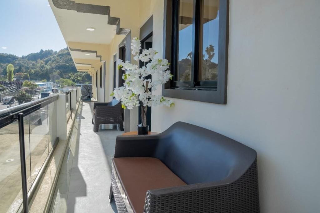 A balcony with a wicker sofa and a vase of white flowers.