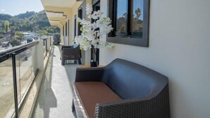A balcony with a wicker sofa and a vase of white flowers.