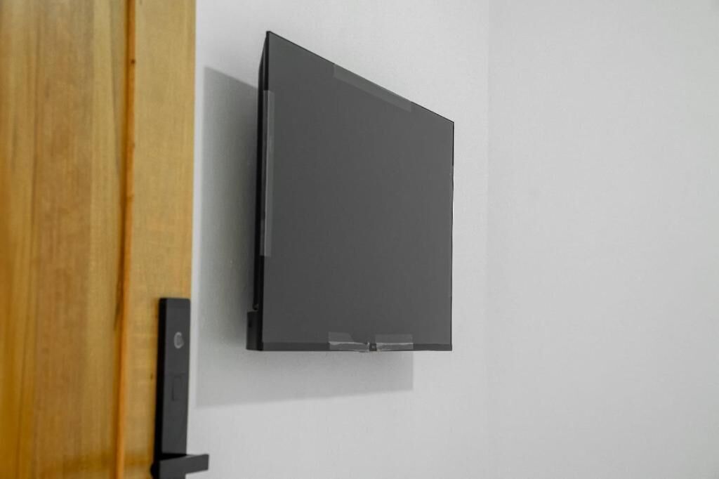 A flat-screen TV mounted on a wall with a wooden door frame to the left.