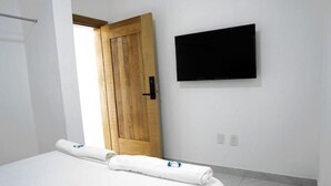 A hotel room with a bed, a wooden door, a flat-screen TV mounted on the wall, and a white towel on the bed.