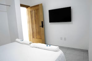 Habitación de hotel con cama, puerta de madera, televisor de pantalla plana montado en la pared y una toalla blanca sobre la cama.