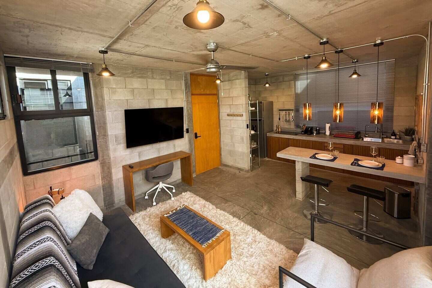 A modern living space with a flat-screen TV, a wooden bench, a sofa, and a kitchen area with bar stools.