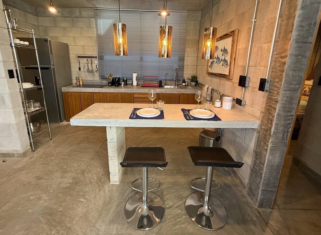 Una cocina moderna con una isla central, taburetes de bar, electrodomésticos de acero inoxidable e iluminación colgante.