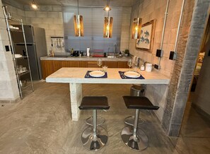 Una cocina moderna con una isla central, taburetes de bar, electrodomésticos de acero inoxidable e iluminación colgante.