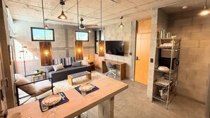 A modern kitchen with a dining area, a sofa, and a TV mounted on the wall.