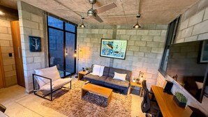Ein modernes Wohnzimmer mit einer Couch, einem Couchtisch und einem Fernseher. Ein Kamin und ein großes Fenster sind ebenfalls vorhanden.
