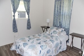 A bedroom with a bed, a bedside table, a lamp, and a window with curtains.