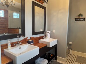 Uma casa de banho com duas pias, um espelho, um candeeiro e um porta-toalhas.
