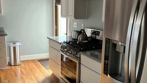 Una cocina moderna con electrodomésticos de acero inoxidable, piso de madera y armarios blancos.