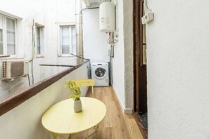 Ein schmaler Balkon mit einem kleinen Tisch und einer Vase mit gelben Blumen, einer Waschmaschine und einer Klimaanlage.