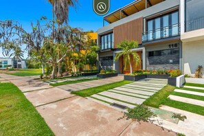 A modern building with a flat roof, large windows, and a paved walkway with grass and plants. - 4BR B-nayar Brisas 116 Mountain Views, Pool (Bucerías)