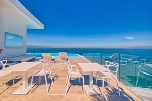 A modern outdoor terrace with a pool, white furniture, and a clear view of the ocean. - Luxurious 2BR Condo - Amazing Ocean View - Pool (Puerto Vallarta)
