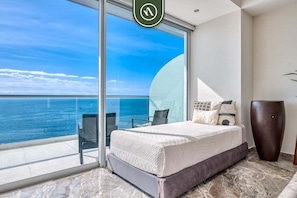 A bedroom with a large bed, a view of the ocean, a glass door, and a tall vase. - Beachview Luxury 3 BR Condo - Pools - Beach (Puerto Vallarta)