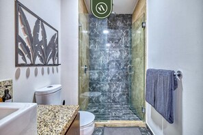 Ein Badezimmer mit Duschkabine aus Glas, Toilette und Waschbecken mit Granitplatte.