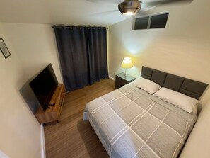 A bedroom with a bed, bedside lamp, and a TV on a wooden stand. - Ensenada 4br/2ba Beach House Pool, Hot Tub, Kayaks (Ensenada)