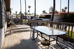 A wooden deck with a glass table and metal chairs, overlooking a residential area with palm trees and houses. - Ensenada 4br/2ba Beach House Pool, Hot Tub, Kayaks (Ensenada)