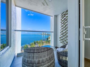 Ein Balkon mit Korbmöbeln, Blick auf das Meer und die Stadtlandschaft.