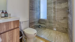 Ein modernes Badezimmer mit einer gläsernen Duschkabine, Toilette und einem Waschtisch mit Pflegeprodukten.