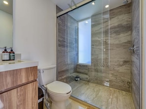 Ein modernes Badezimmer mit einer gläsernen Duschkabine, Toilette und einem Waschtisch mit Pflegeprodukten.