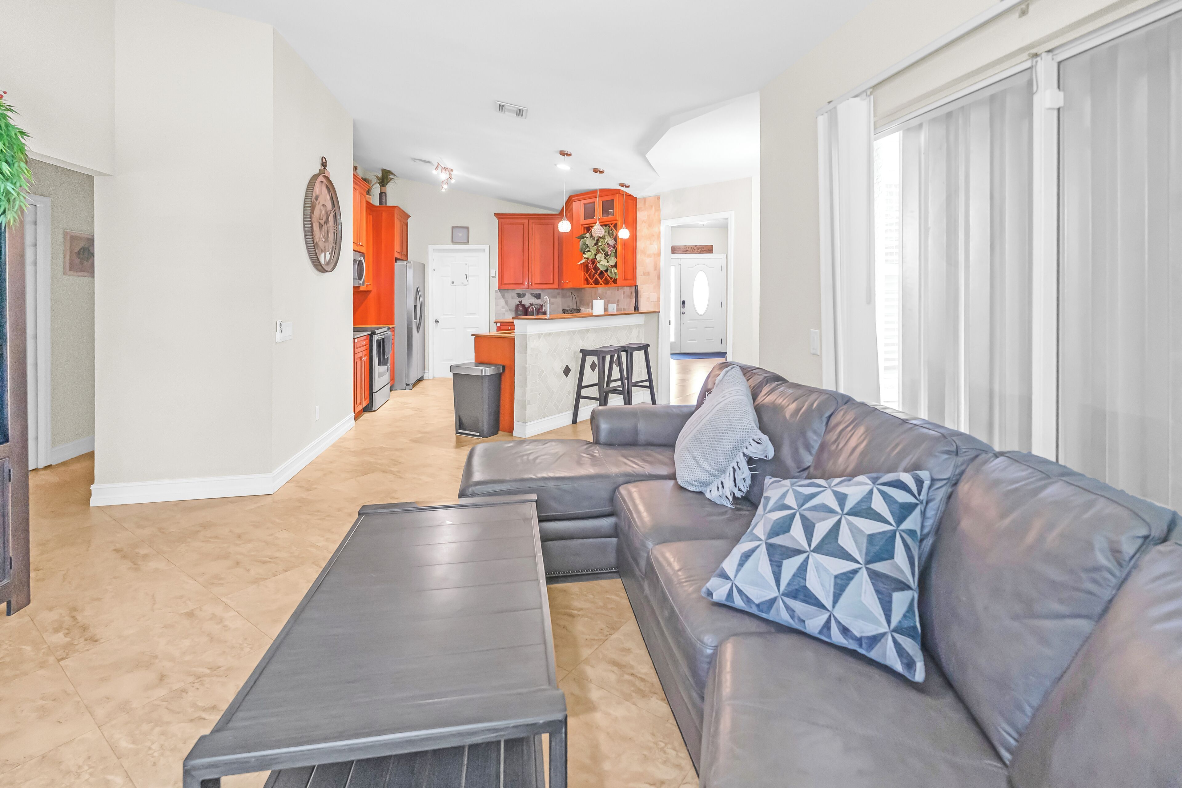 A modern living room with a grey sofa, a coffee table, and a kitchen in the background with orange cabinets.
