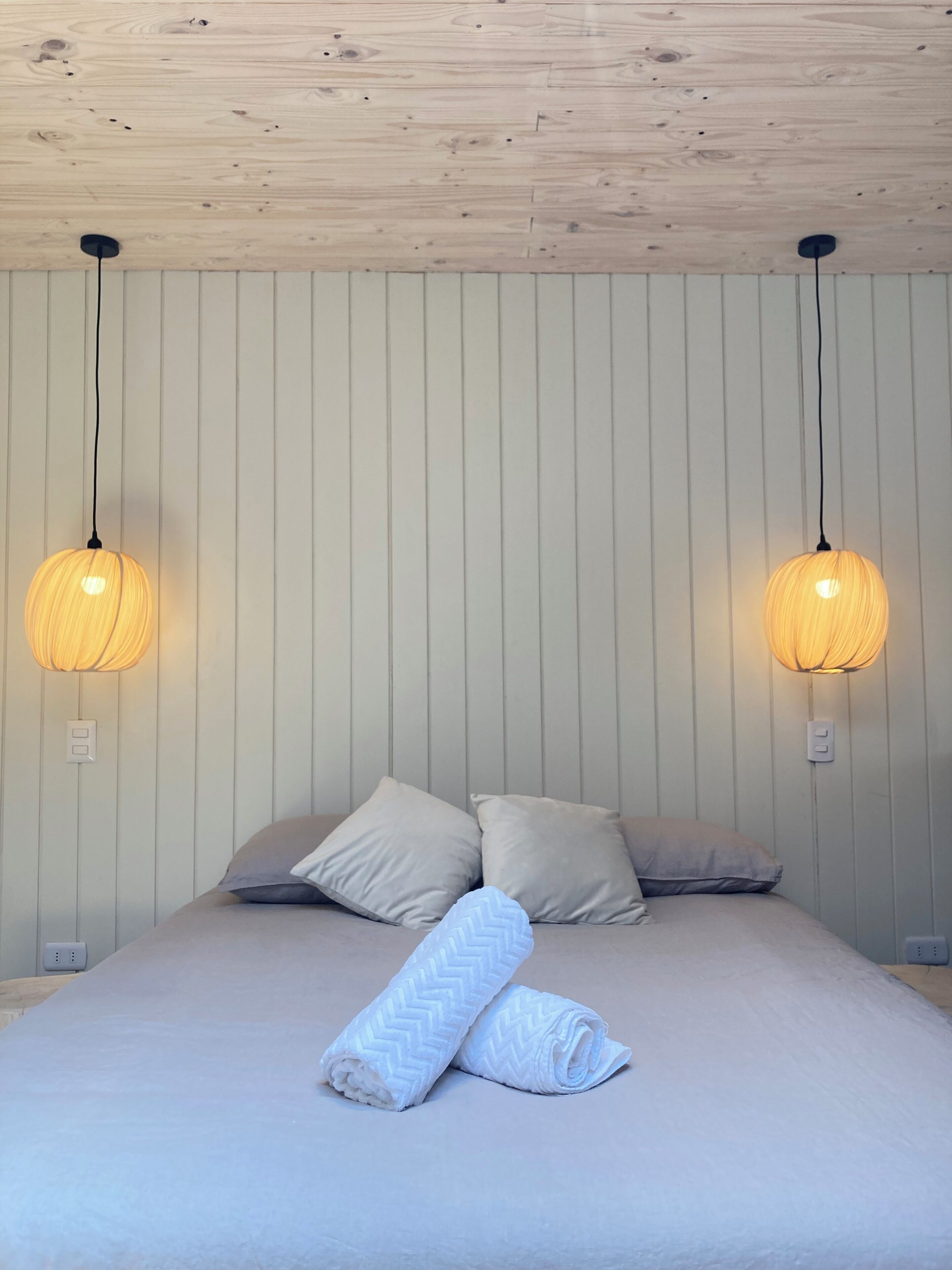 A bedroom with a bed, two wall-mounted lamps, and a wooden ceiling.