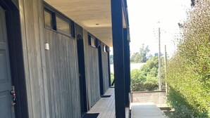 A covered outdoor area with a wooden deck, metal doors, and a pathway leading to a building. - Alba Lodge (Valparaíso)