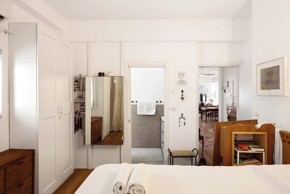 A bedroom with a bed, a wooden dresser, a mirror, a wardrobe, and a small wooden table.