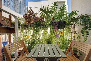An outdoor seating area with a table and chairs, surrounded by lush greenery and flowering plants.