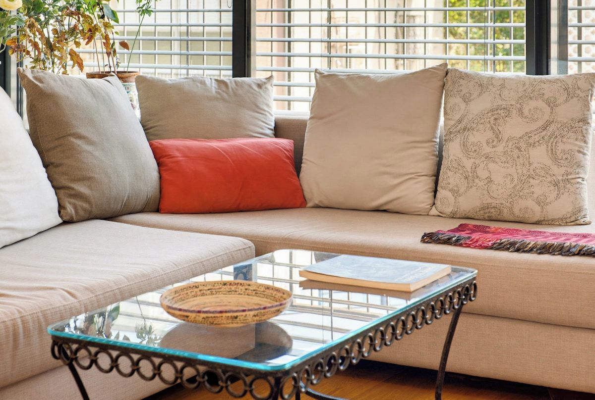 A living room with a sofa, cushions, a glass coffee table, and a book.