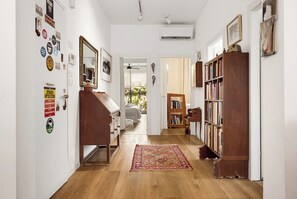 A hallway with a wooden floor, a patterned rug, a bookshelf, and various wall decorations.