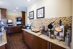 A kitchen area with a waffle maker, a coffee machine, and a Pepsi cooler.