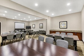 A conference room with a large table, multiple chairs, a projector screen, a television, and framed artwork on the walls.
