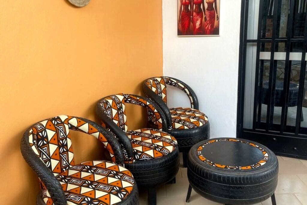 Drie stoelen met geometrische kussens en een kleine ronde tafel, beide met een vergelijkbaar ontwerp, geplaatst tegen een muur met een zwart hek op de achtergrond.
