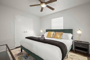 Quarto com cama, mesas de cabeceira, ventilador de teto e janela com persianas.