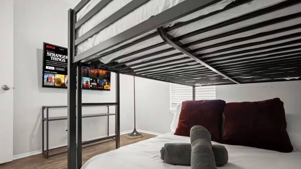 Ein Stockbett mit an der Wand befestigtem Fernseher, einem kleinen Tisch und einem roten Kopfkissen.