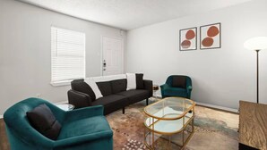 Ein Wohnzimmer mit einer Couch, zwei Sesseln, einem Glastisch und einer Stehlampe.